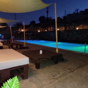 Un espace extérieur avec piscine, des chaises longues et des tables, entouré de murs en pierre et bordé par une colline.