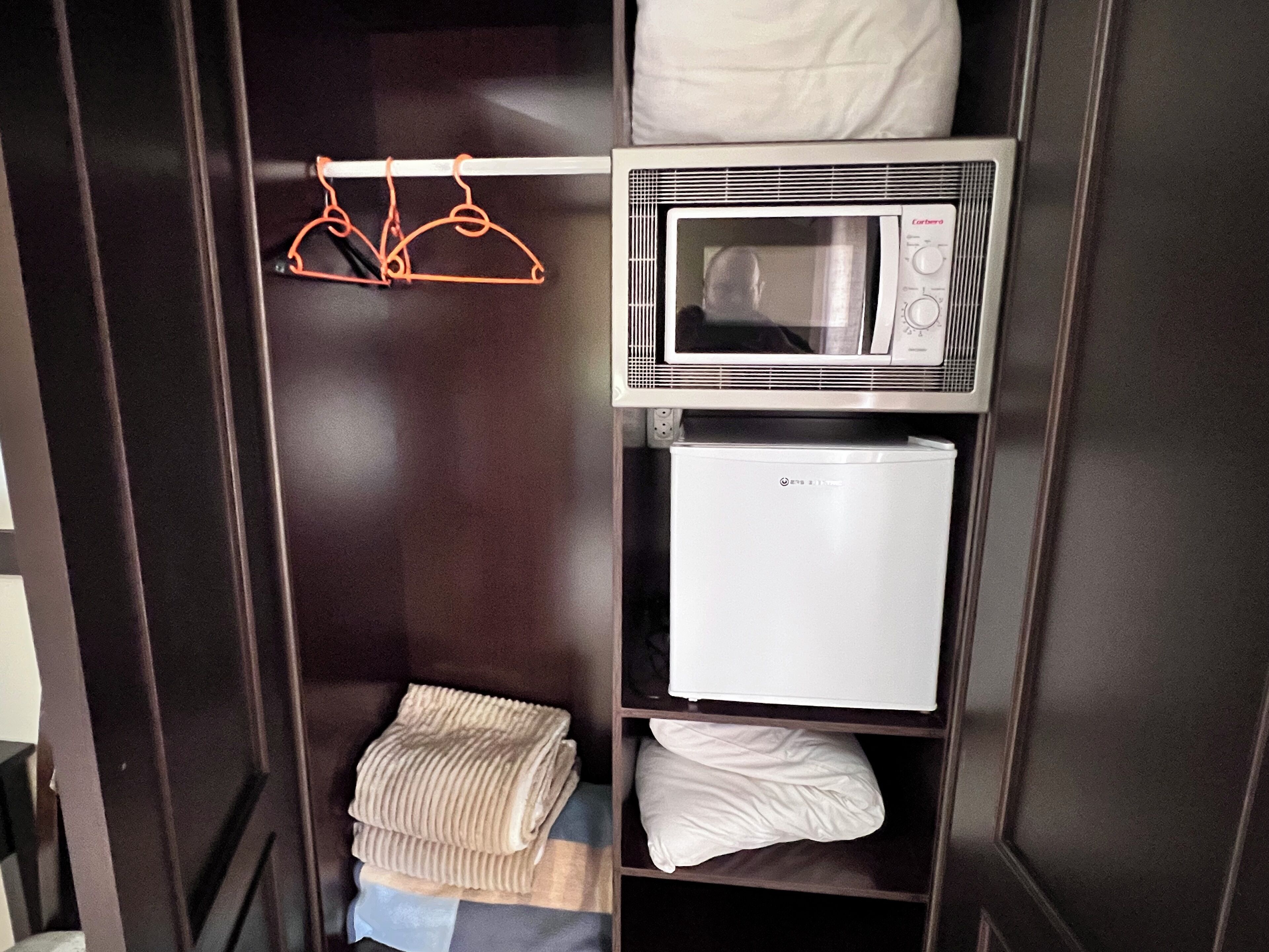 A closet with a microwave, a mini-fridge, and hanging clothes.