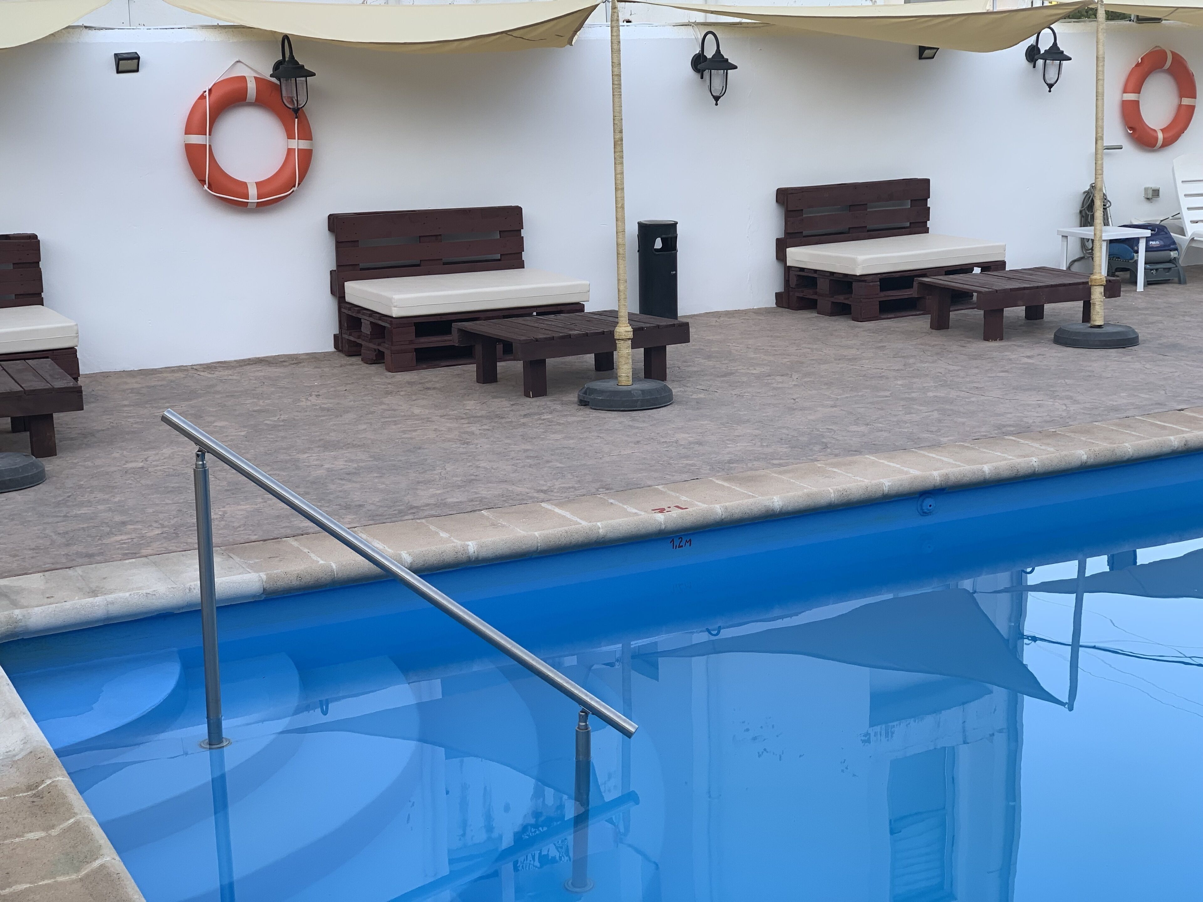A poolside area with wooden benches, a lifebuoy, and a metal railing.
