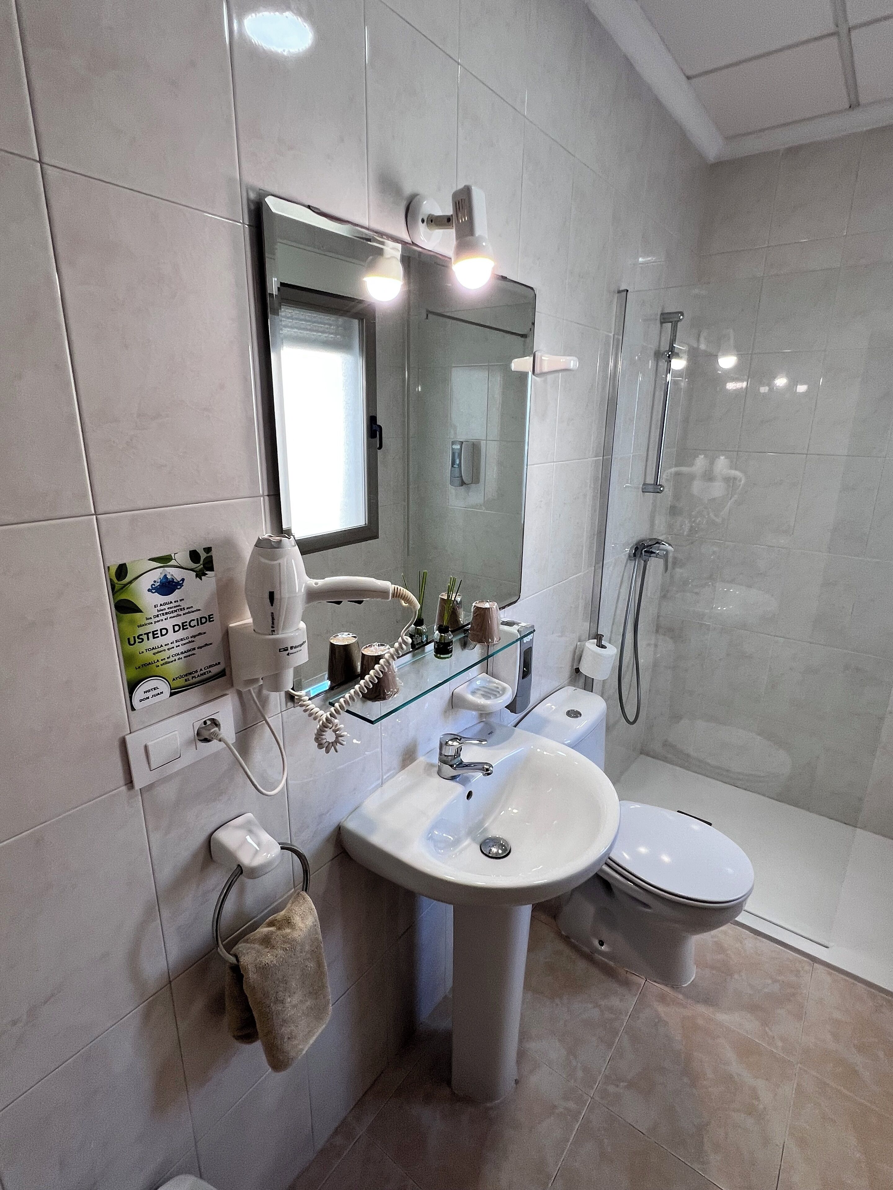 A modern bathroom with a glass shower enclosure, a pedestal sink, a toilet, and a vanity with a mirror.