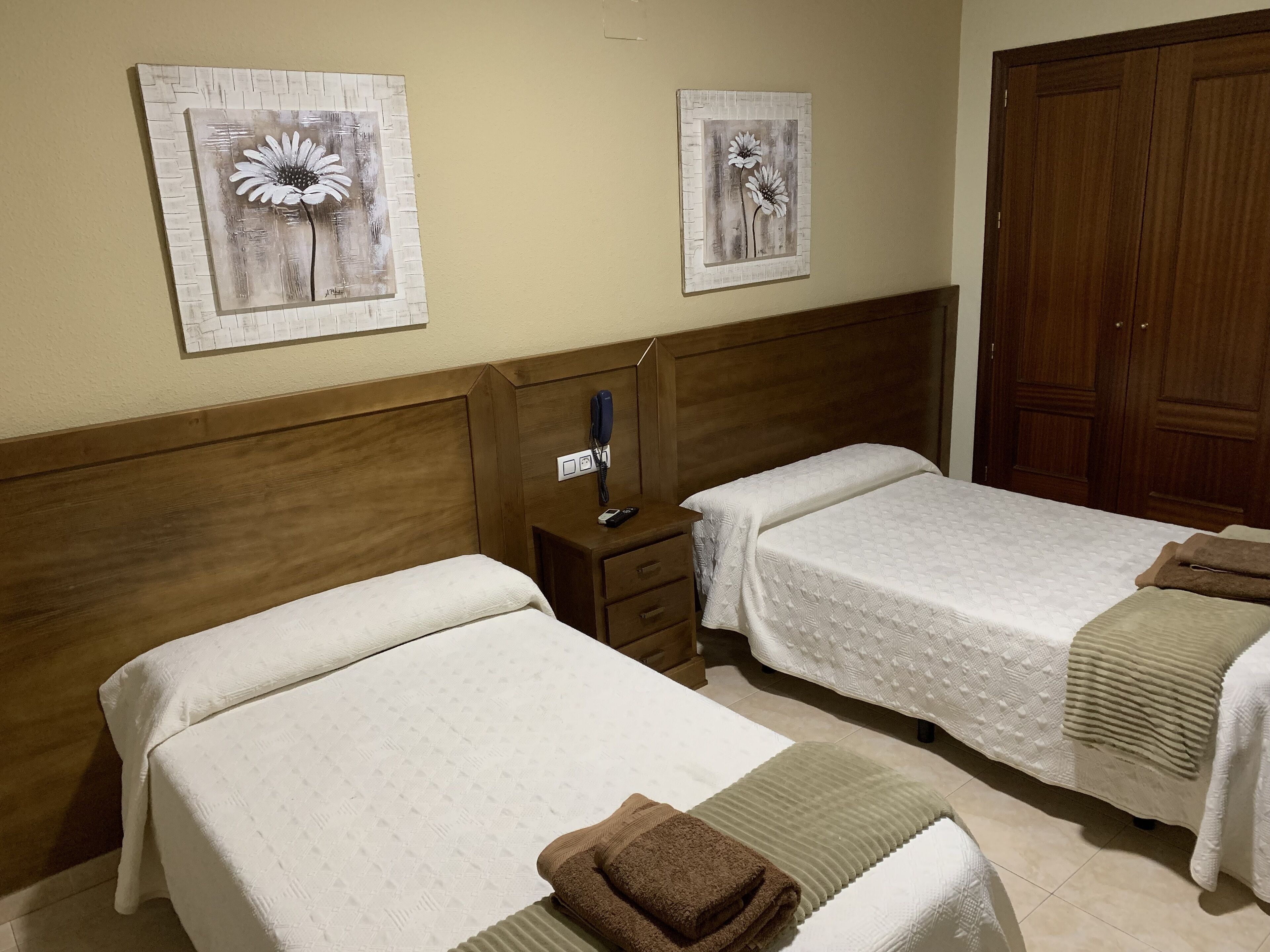 Ein Hotelzimmer mit zwei Betten, einem hölzernen Kopfteil, einem Nachttisch mit Telefon und einem Bild an der Wand.