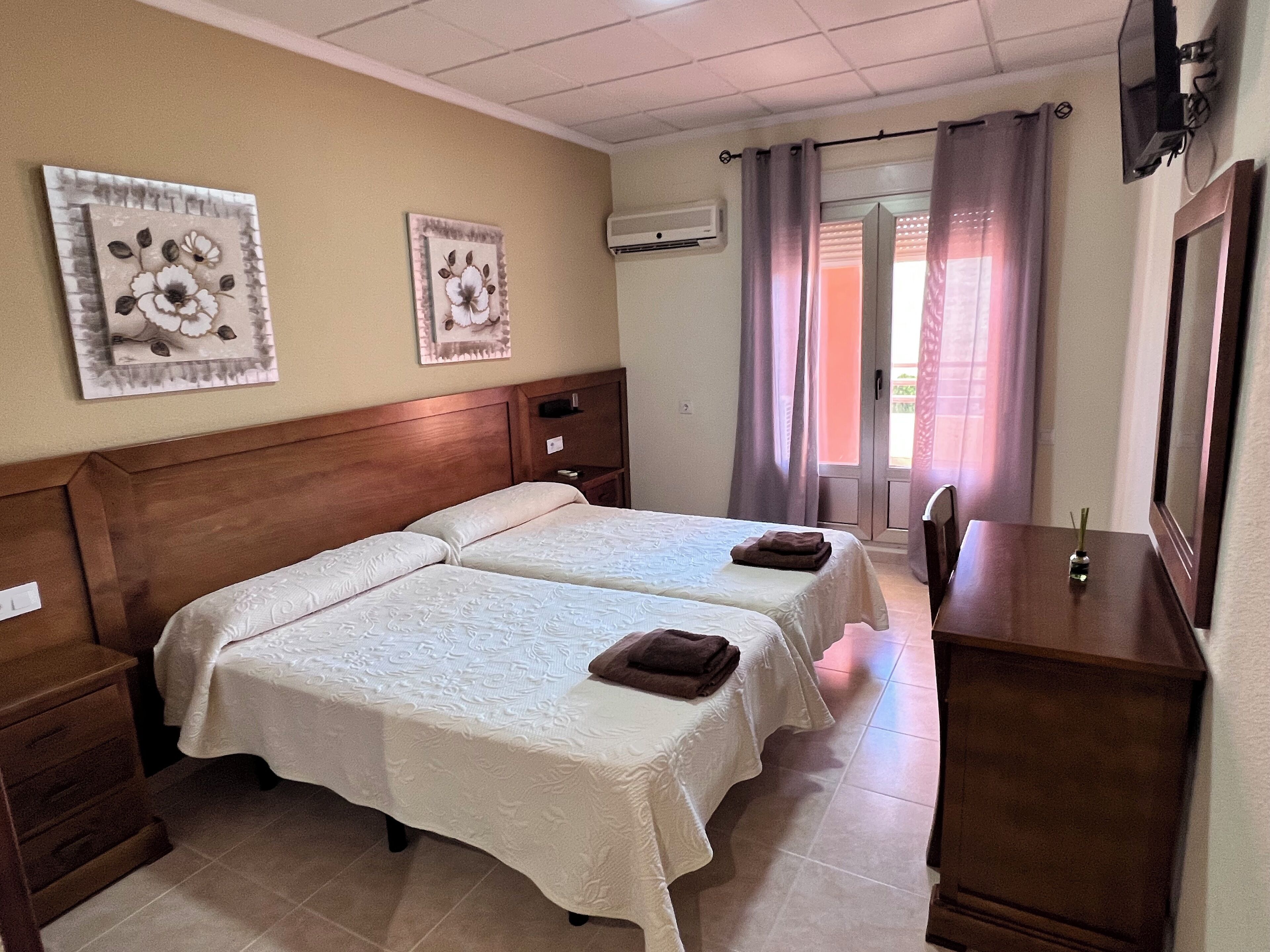 A hotel room with two beds, a wooden dresser, a TV, and artwork on the walls.