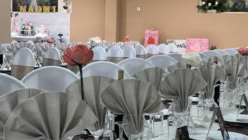 Un salón de banquetes con mesas redondas cubiertas con manteles blancos, cubiertos y cristalería.