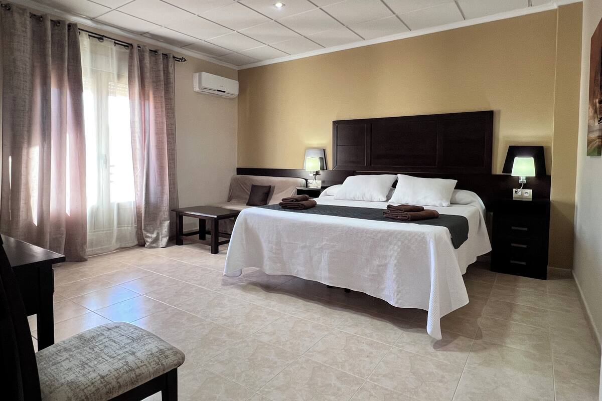 Una habitación de hotel con cama, mesitas de noche, escritorio y una silla.