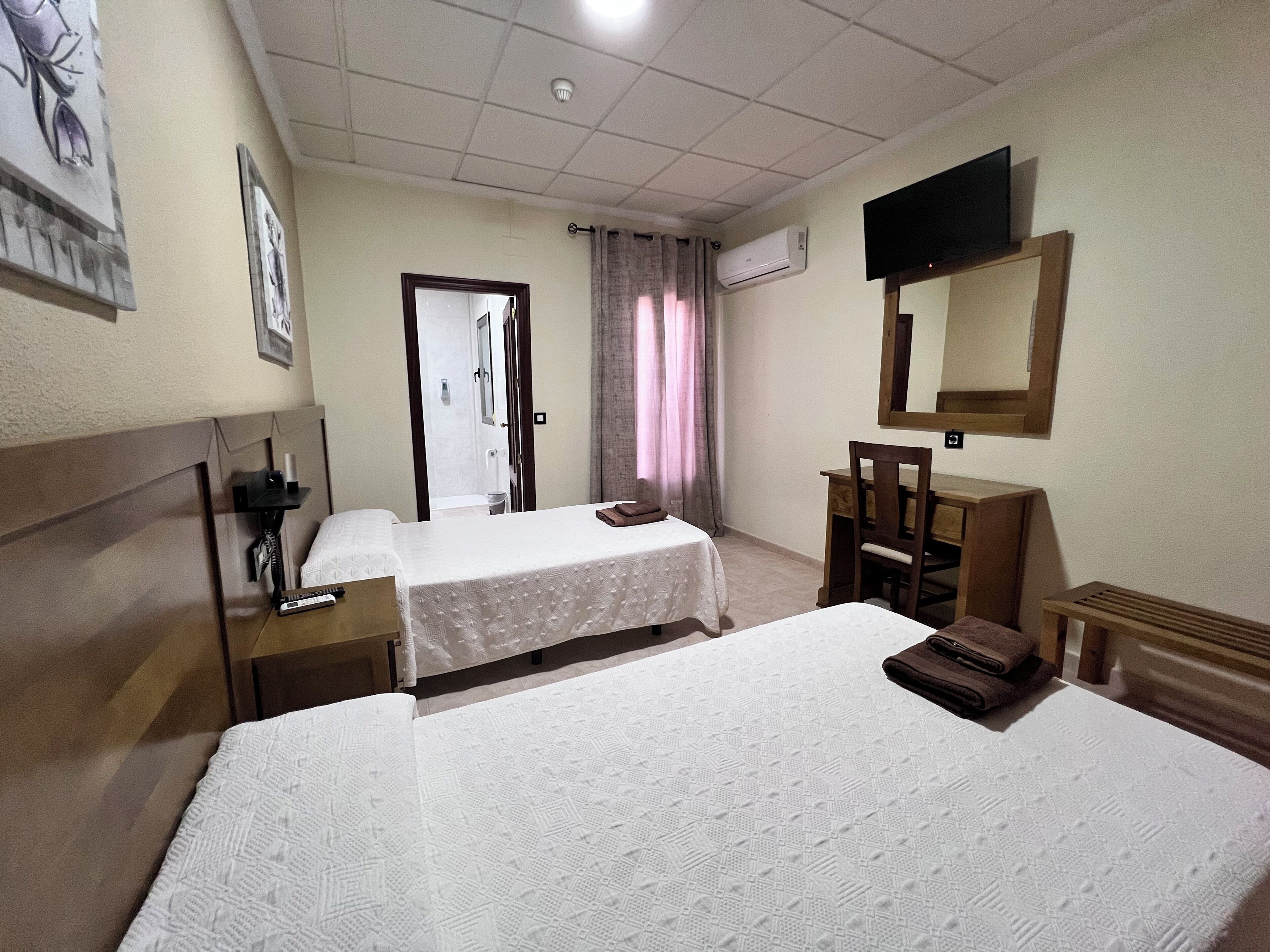 Habitación de hotel con dos camas, un escritorio, una silla, un televisor y aire acondicionado.