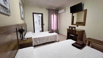 Quarto de hotel com duas camas, uma escrivaninha, uma cadeira, uma televisão e um ar condicionado.