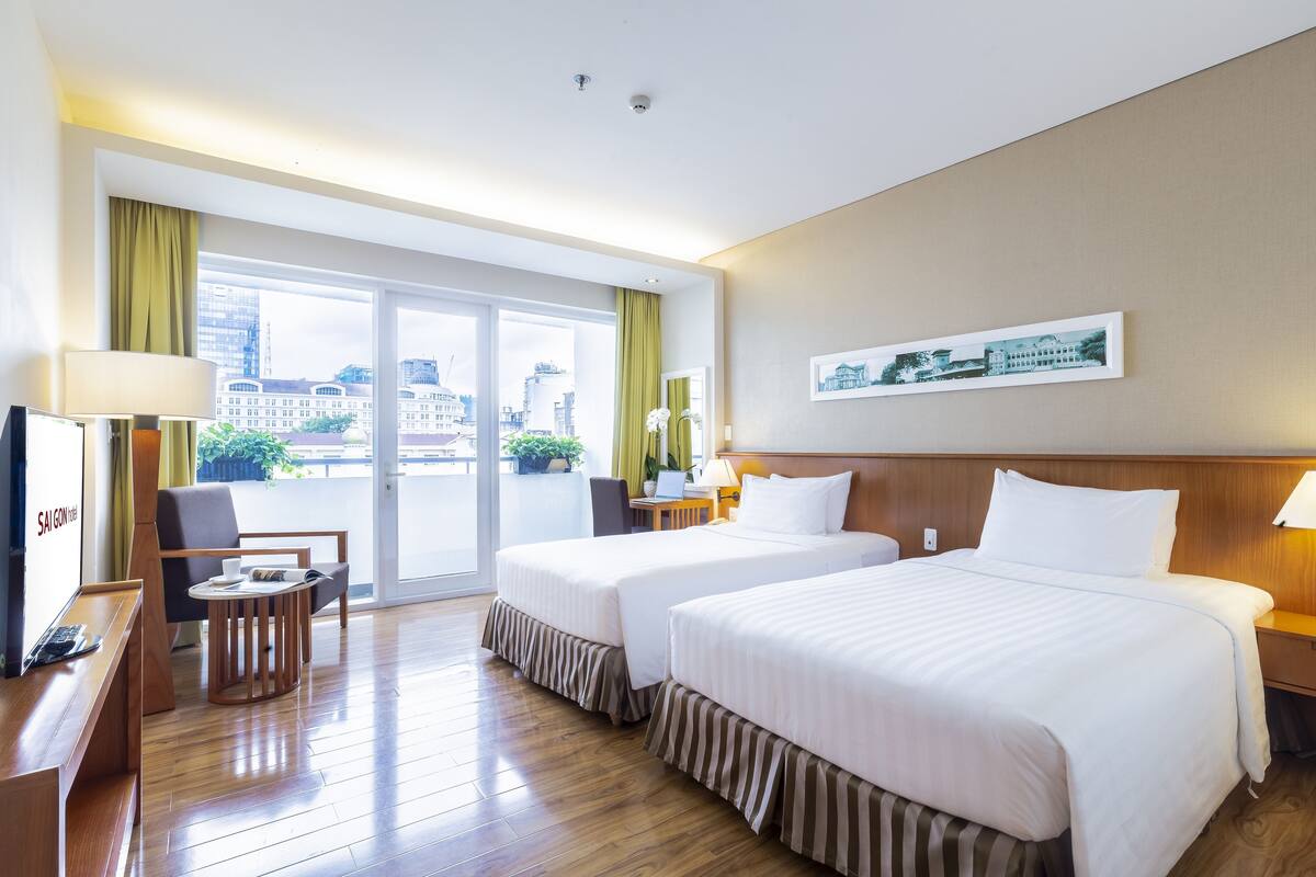 Une chambre d’hôtel avec deux lits, un bureau avec un ordinateur, une chaise, une petite table et une vue sur la ville grâce à de grandes fenêtres.