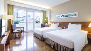 Une chambre d’hôtel avec deux lits, un bureau avec un ordinateur, une chaise, une petite table et une vue sur la ville grâce à de grandes fenêtres.