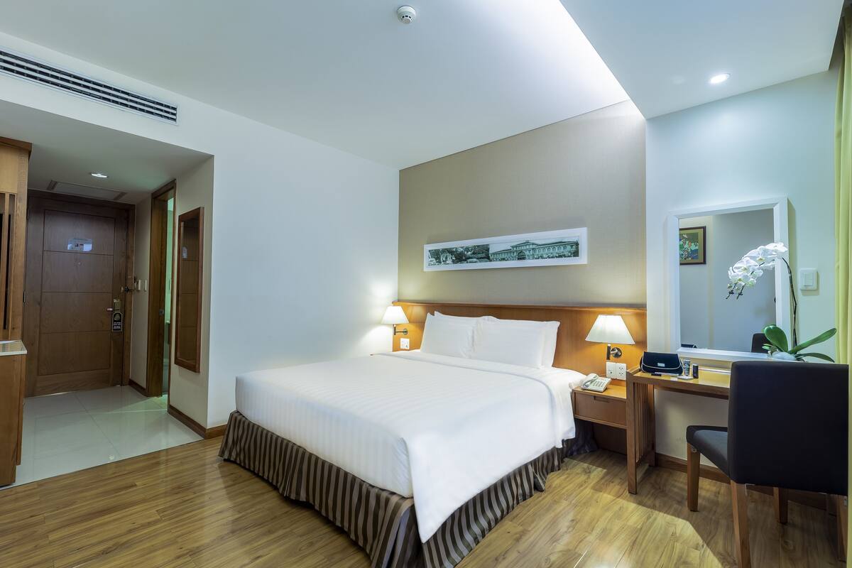 Une chambre d’hôtel avec un grand lit, des tables de chevet avec des lampes, un bureau avec une chaise, un miroir et un tableau au mur.