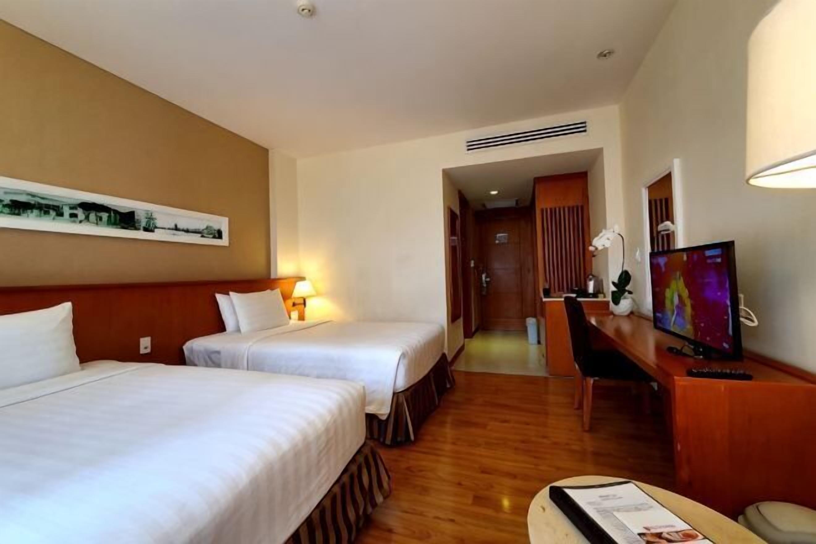 Ein Hotelzimmer mit zwei Betten, einem Schreibtisch, einem Fernseher und einem gerahmten Bild an der Wand.