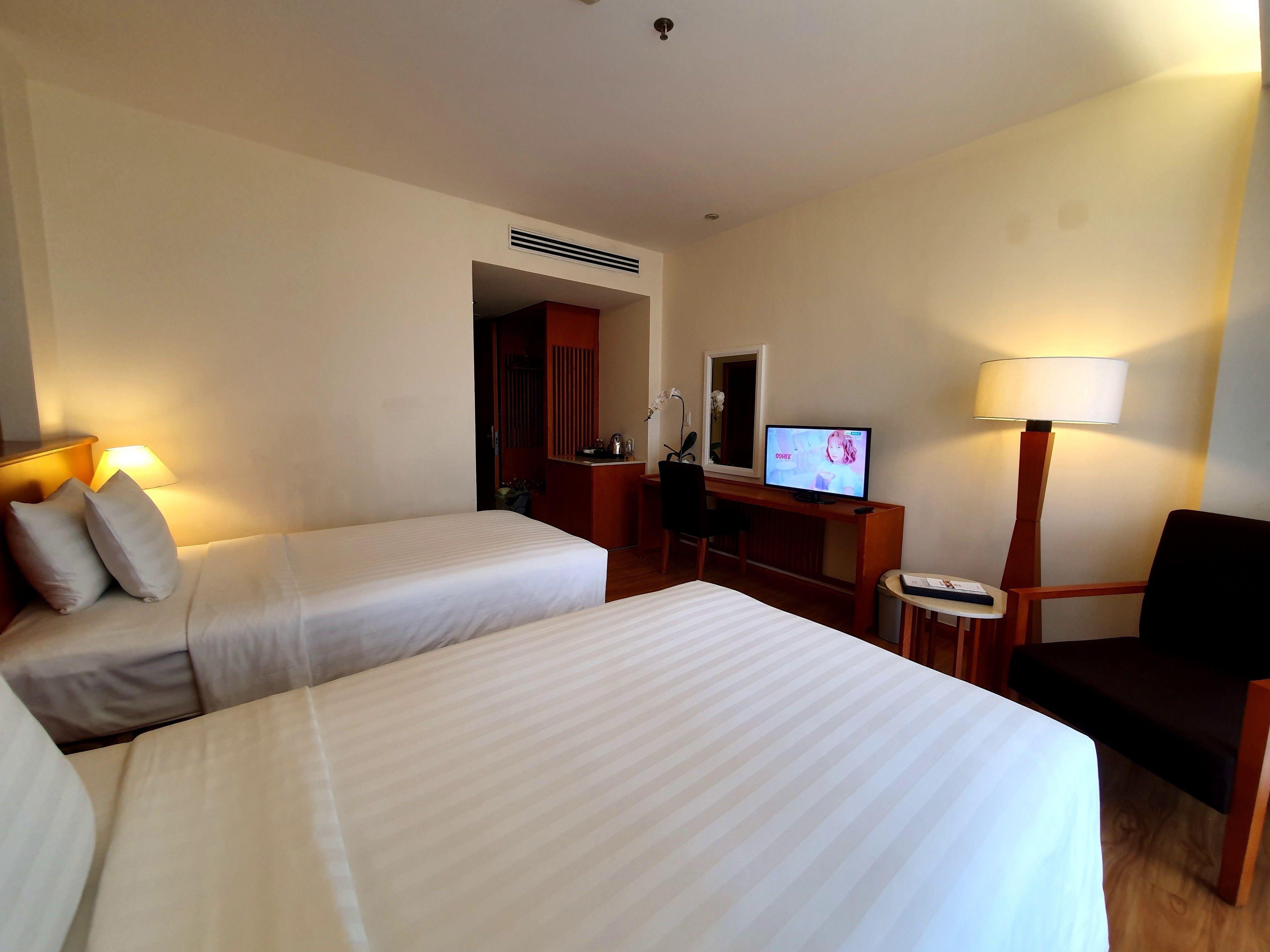 A hotel room with two beds, a desk with a computer, a chair, a lamp, and a small table.