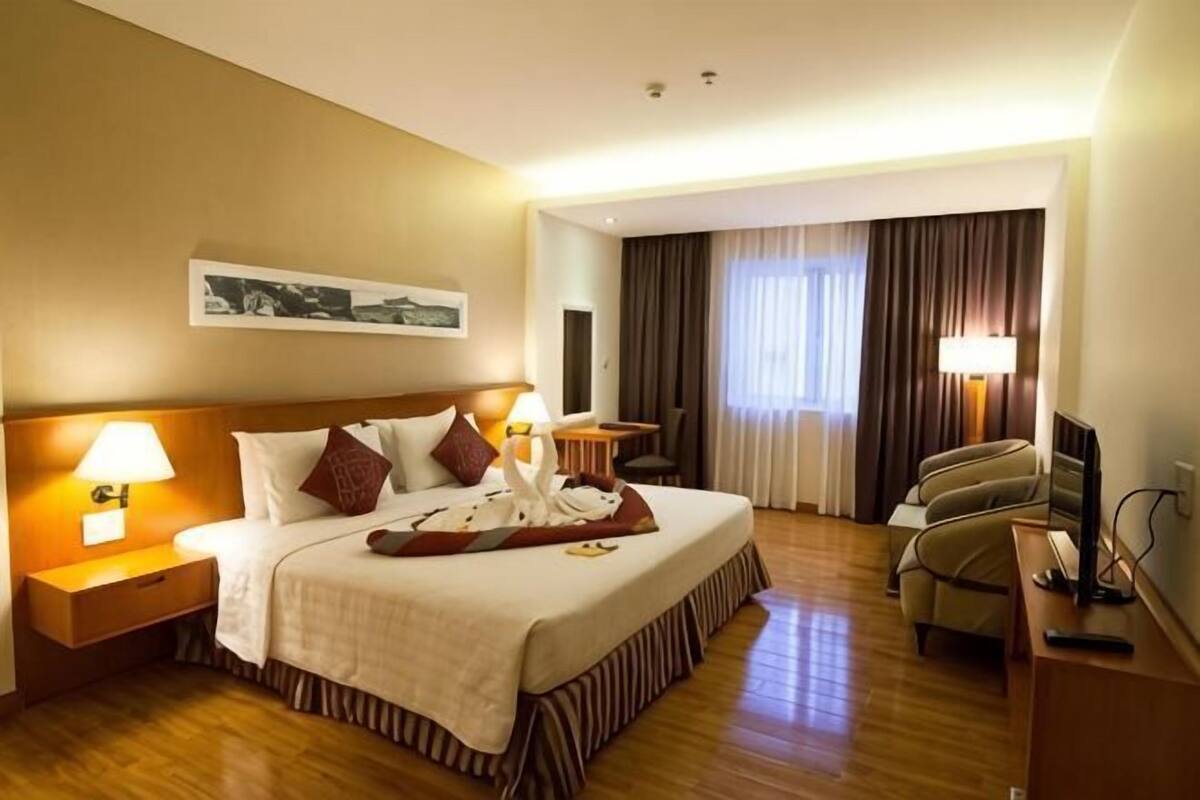 Une chambre d’hôtel avec un lit, des lampes de chevet, un bureau, une chaise, une télévision et une fenêtre avec des rideaux.