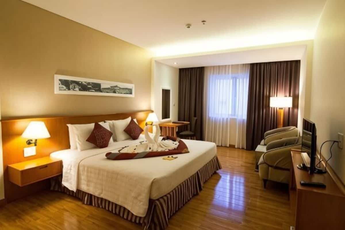 Ein Hotelzimmer mit Bett, Nachttischlampen, Schreibtisch, Stuhl, Fernseher und einem Fenster mit Vorhängen.