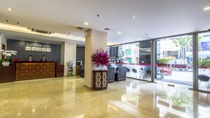 Un espace d’accueil d’hôtel au design moderne, comprenant un comptoir d’accueil, un coin salon et de grandes fenêtres donnant sur la rue.