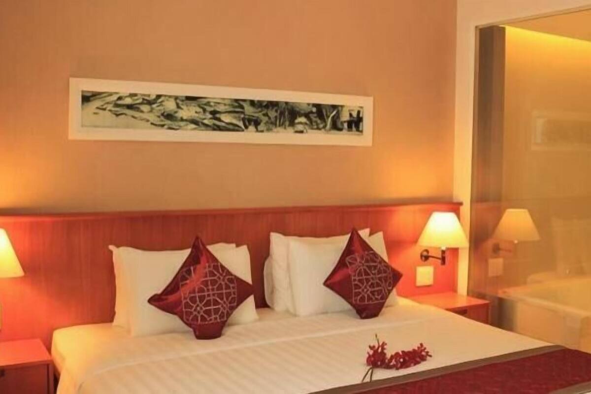 Une chambre d’hôtel avec un lit, deux tables de chevet, une lampe fixée au mur, un tableau et un miroir.