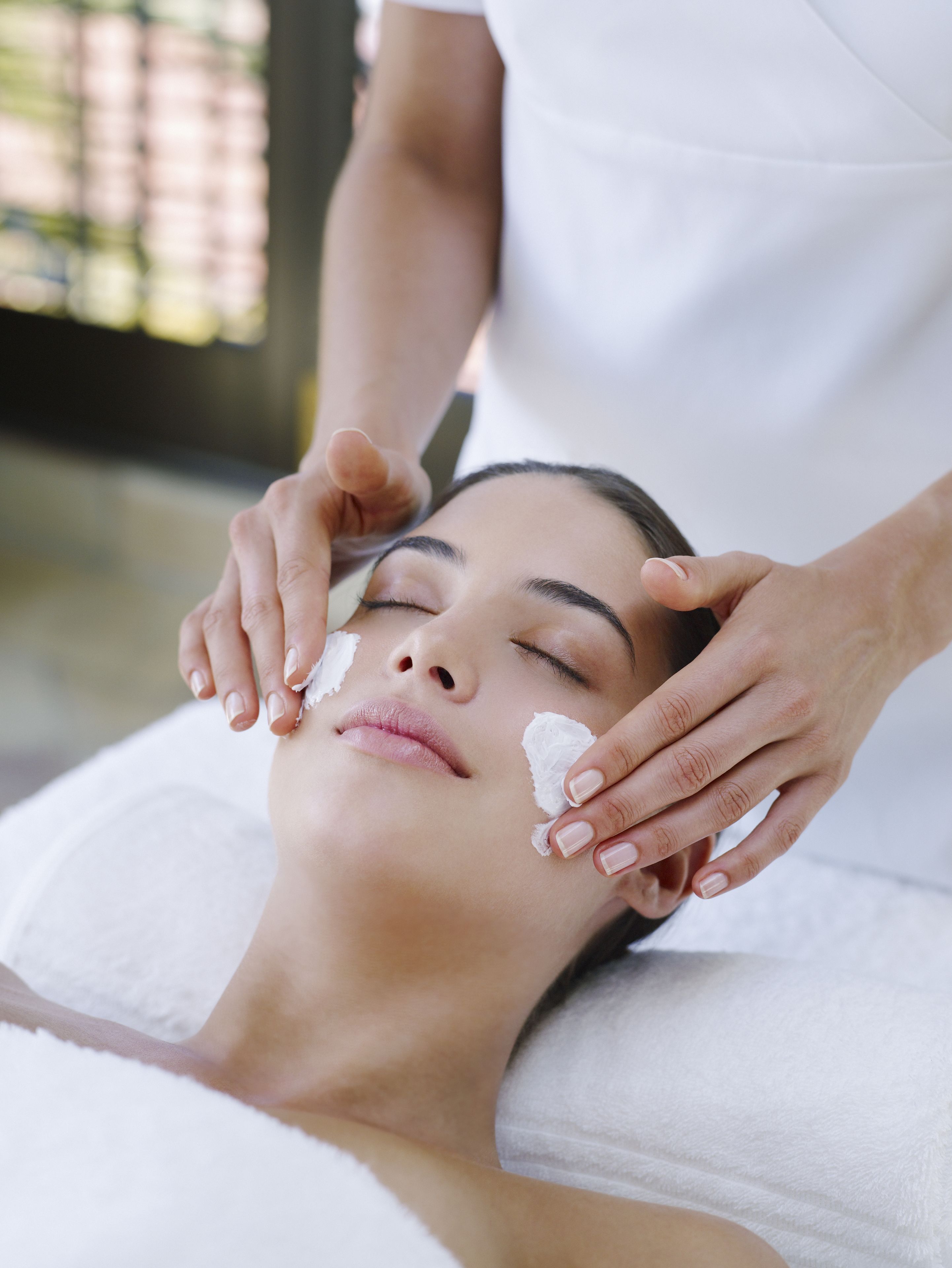 A person receiving a facial treatment with a white towel covering their head.