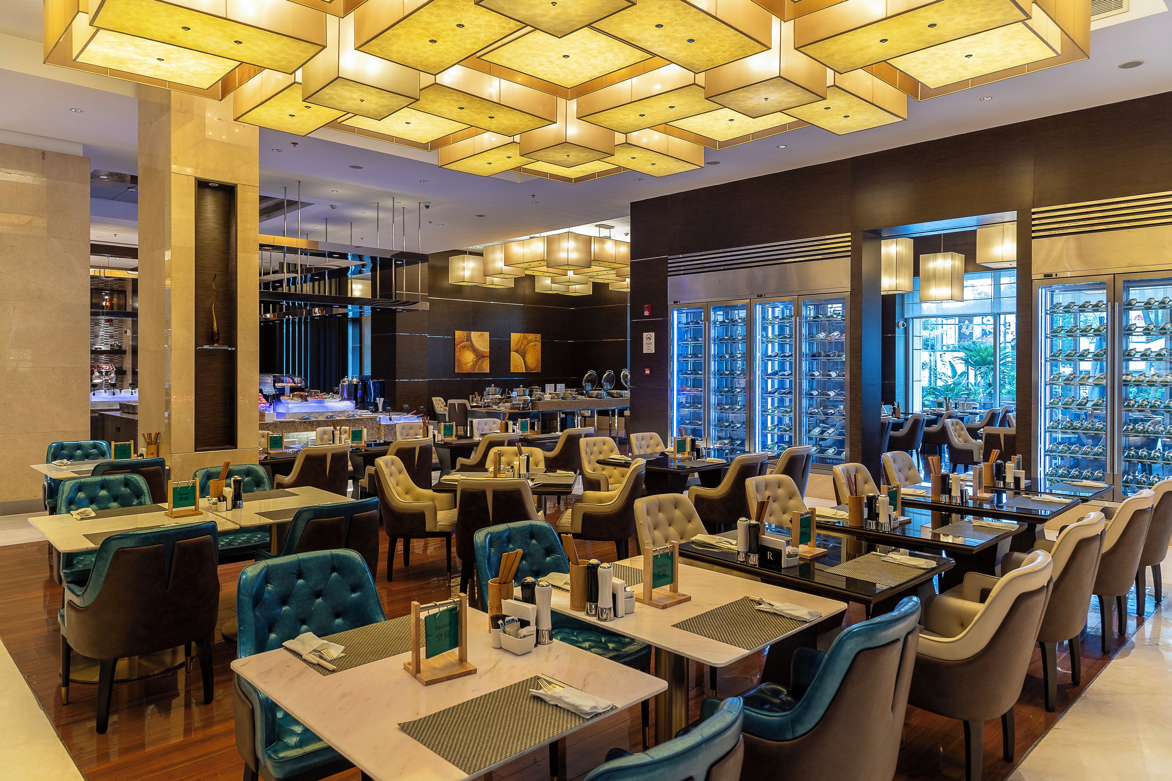 Um restaurante com várias mesas e cadeiras, um espaço de bar e vista para o exterior através de grandes janelas.