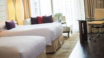 A hotel room with two beds, a desk, a chair, a lamp, and a view of the city.