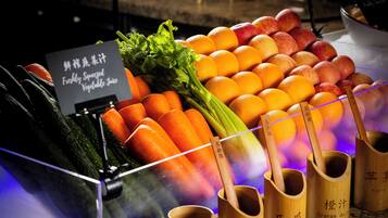 Presentatie van verse groenten en fruit, waaronder wortelen, selderij, sinaasappels en appels, met houten bakken voorzien van labels voor verschillende soorten sap.