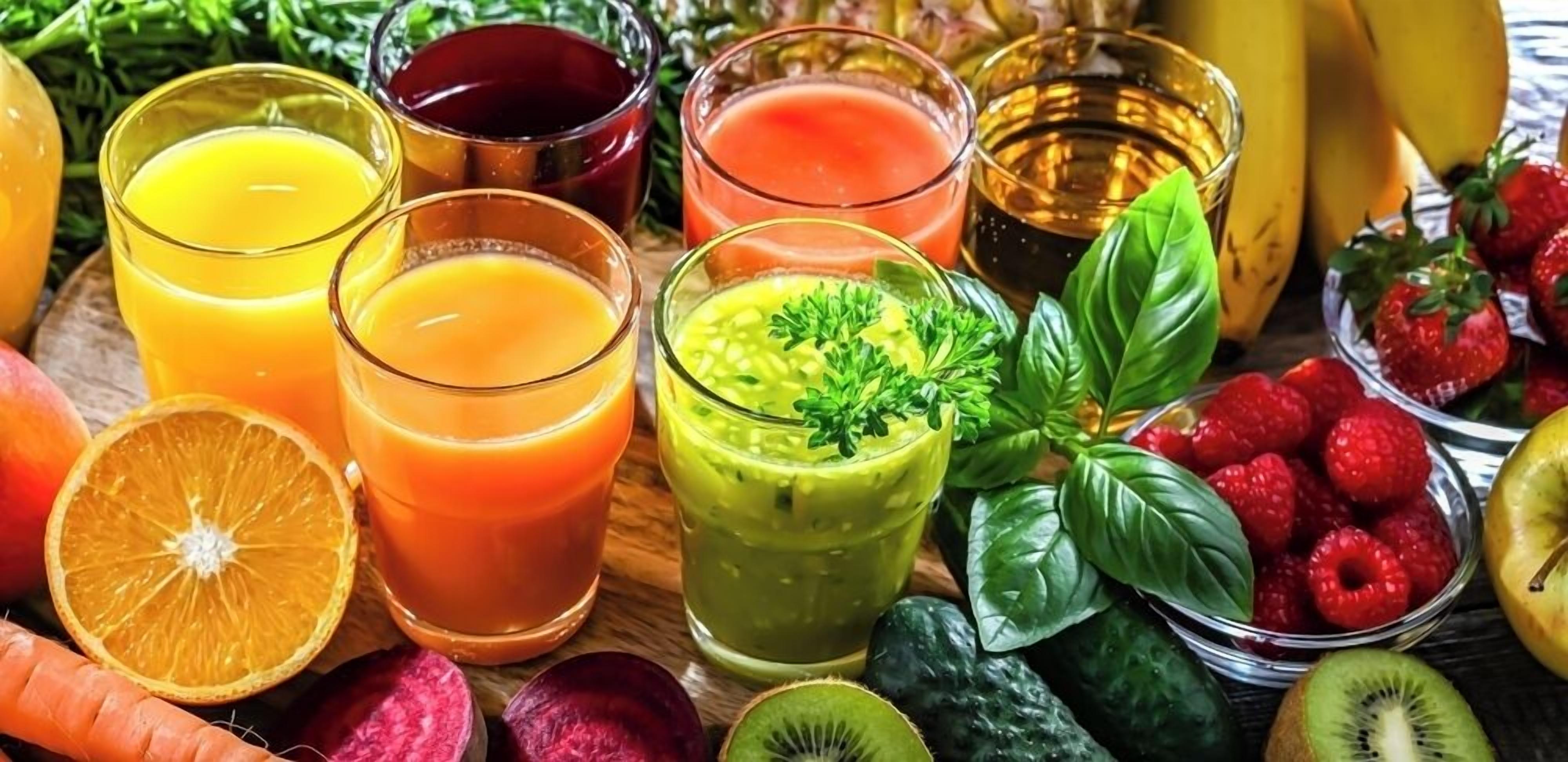 A variety of fresh fruits and colorful beverages, likely juices or smoothies, arranged on a wooden surface.