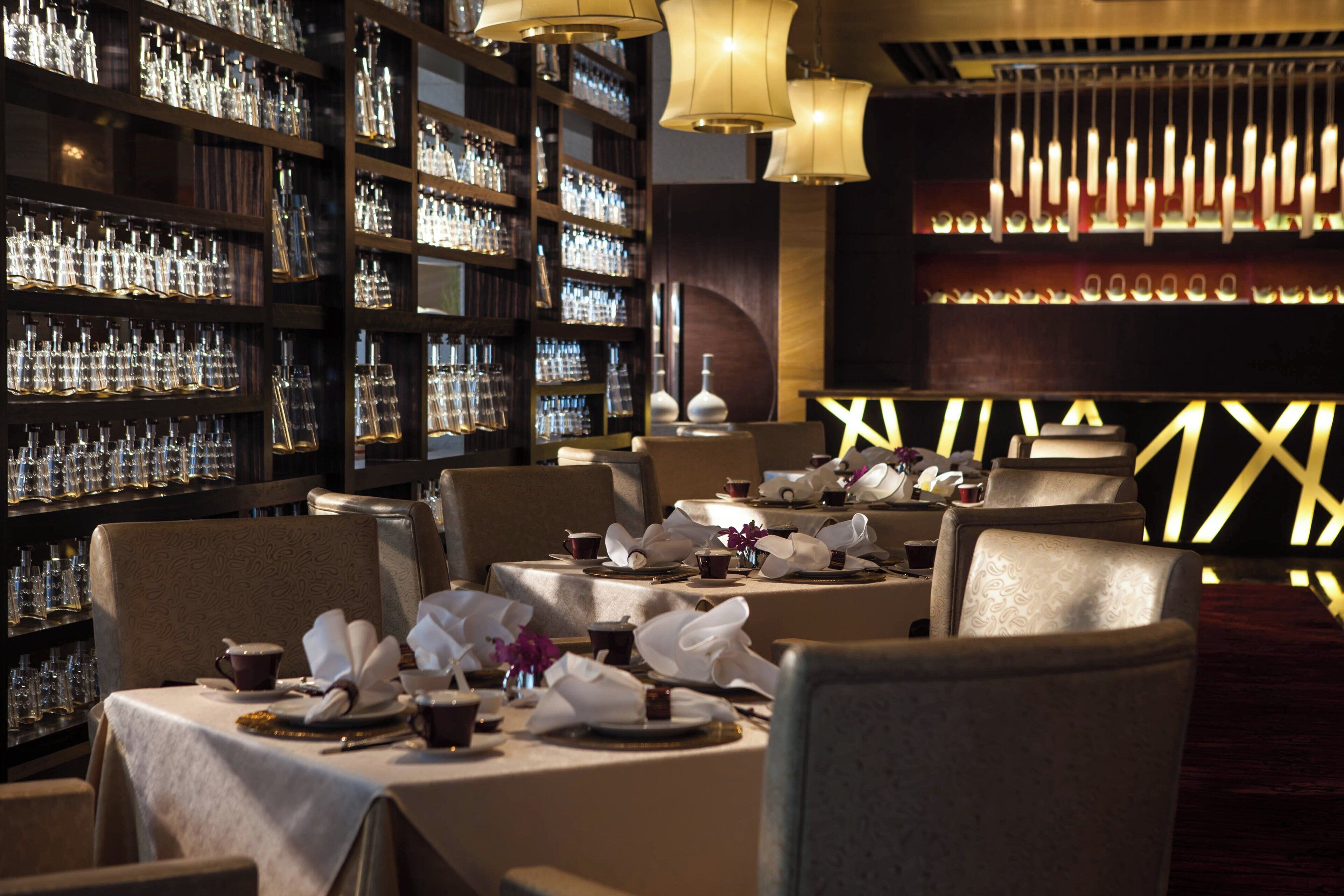 A restaurant with tables set for dining, a bar area with bottles, and a decorative wall with a geometric pattern.