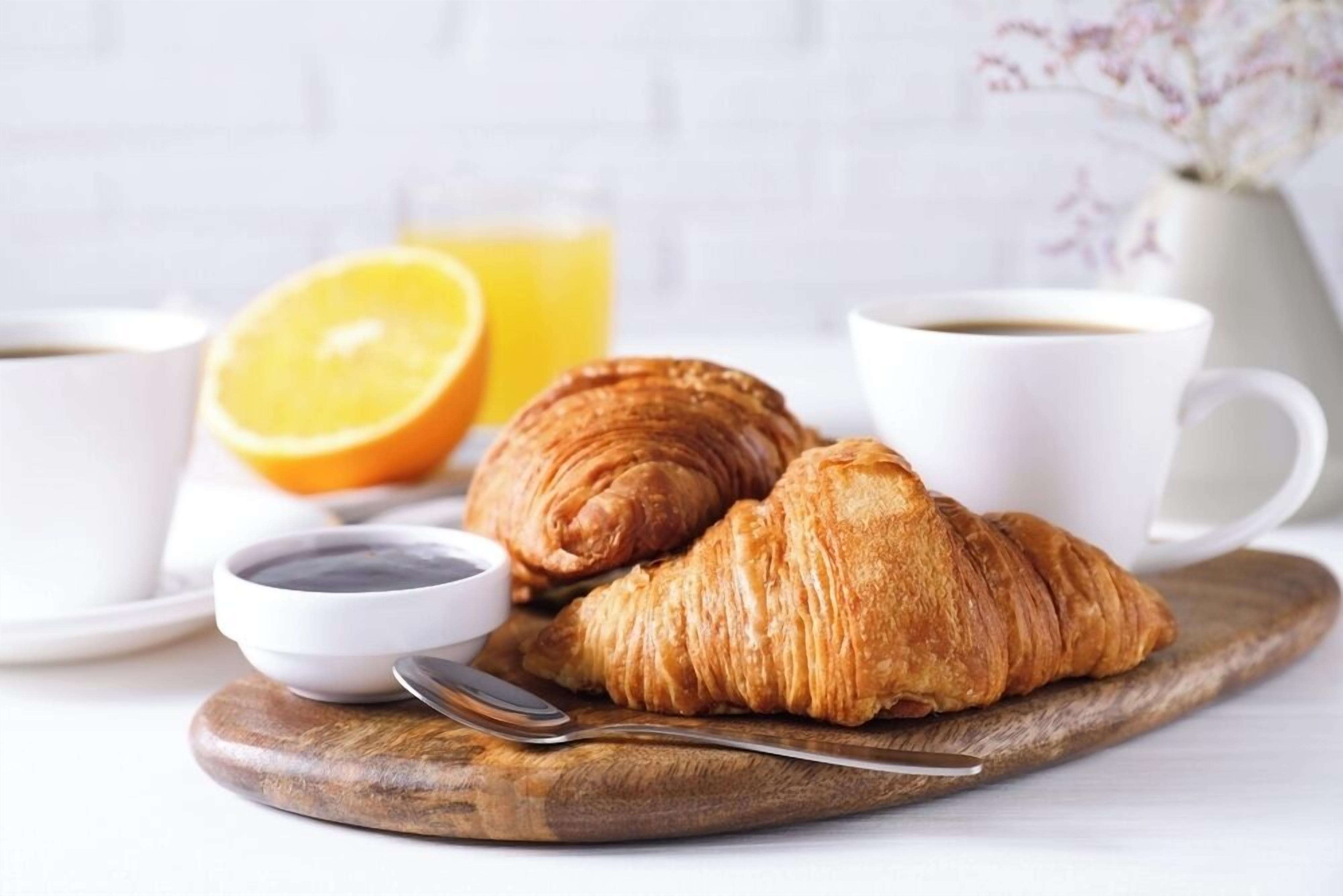 A croissant on a wooden board, a cup of coffee, a half orange, and a small bowl of jam.