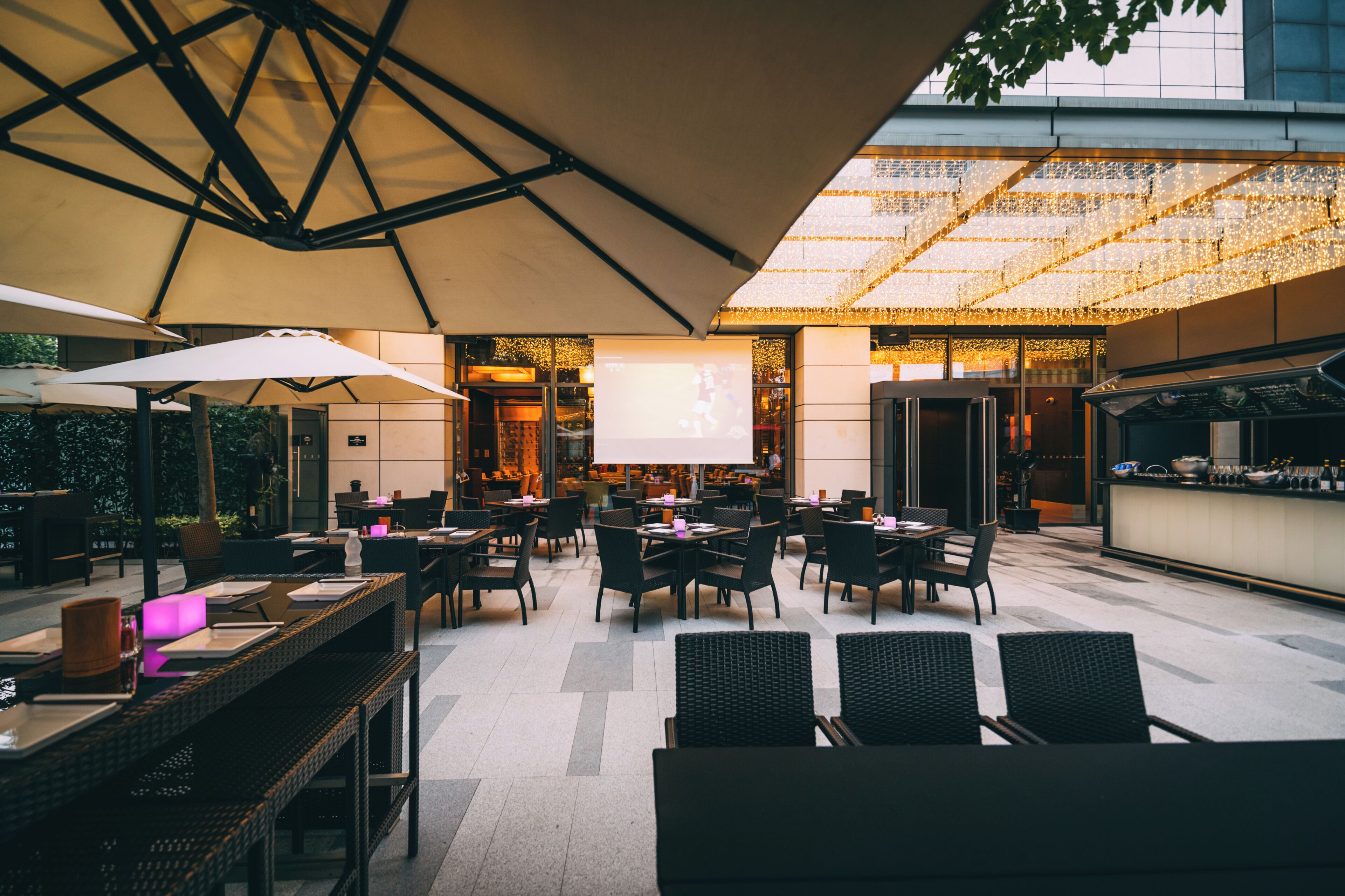 An outdoor dining area with tables and chairs, umbrellas, and a projection screen.