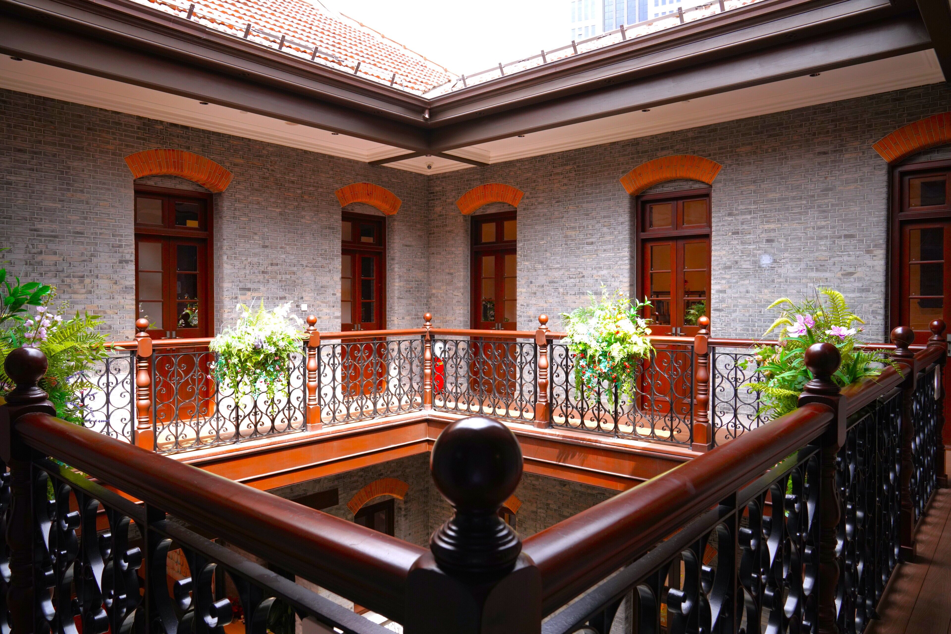Un patio con pared de ladrillo, puertas de madera y barandilla de balcón.