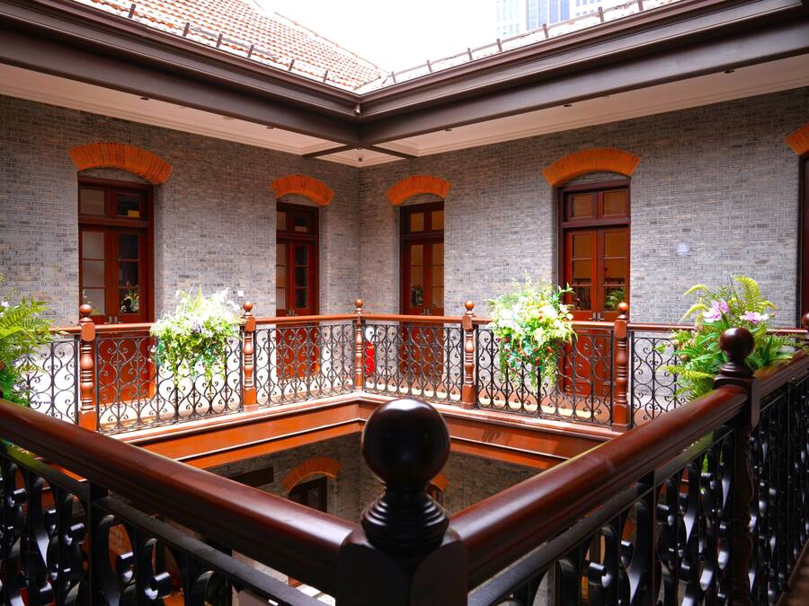 Un patio con pared de ladrillo, puertas de madera y barandilla de balcón.