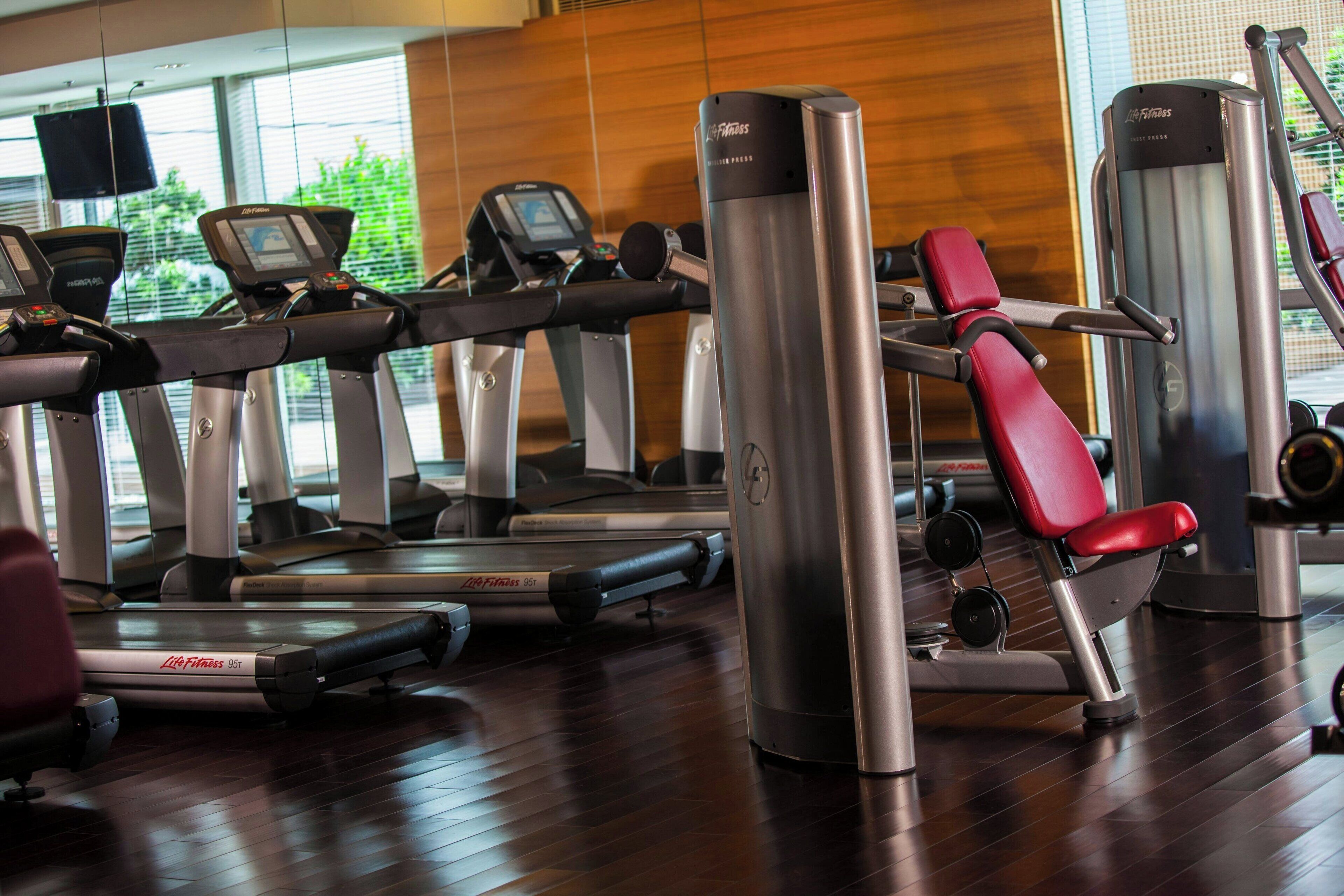 Een fitnessruimte met loopbanden, krachtapparaten en een rode trainingsstoel.