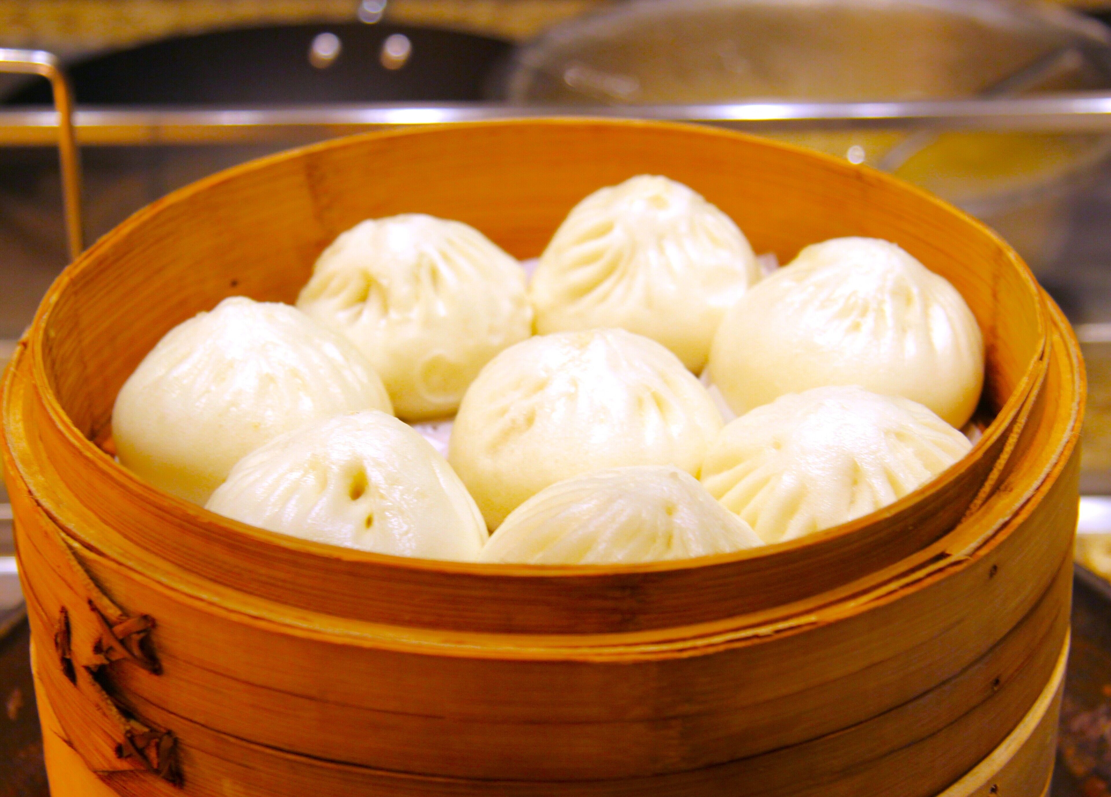 A bamboo steamer basket containing several white steamed buns.