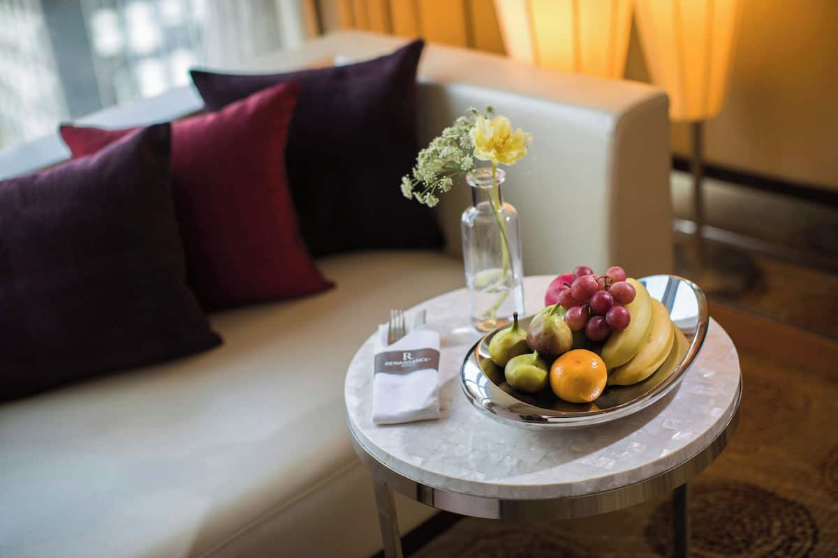 A dining table with a fruit bowl, a vase with flowers, and a napkin with a logo.