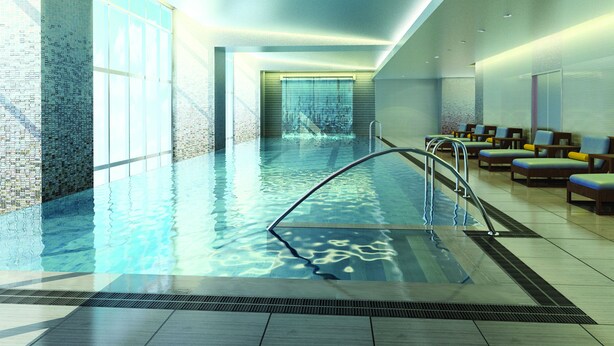 Una piscina interior moderna con agua cristalina, una escalera metálica y sillas de descanso a un lado.