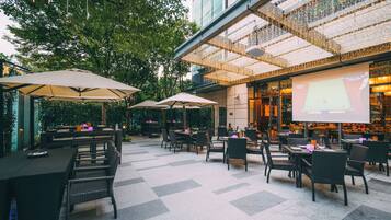 An outdoor seating area with tables and chairs, umbrellas, and a projection screen.