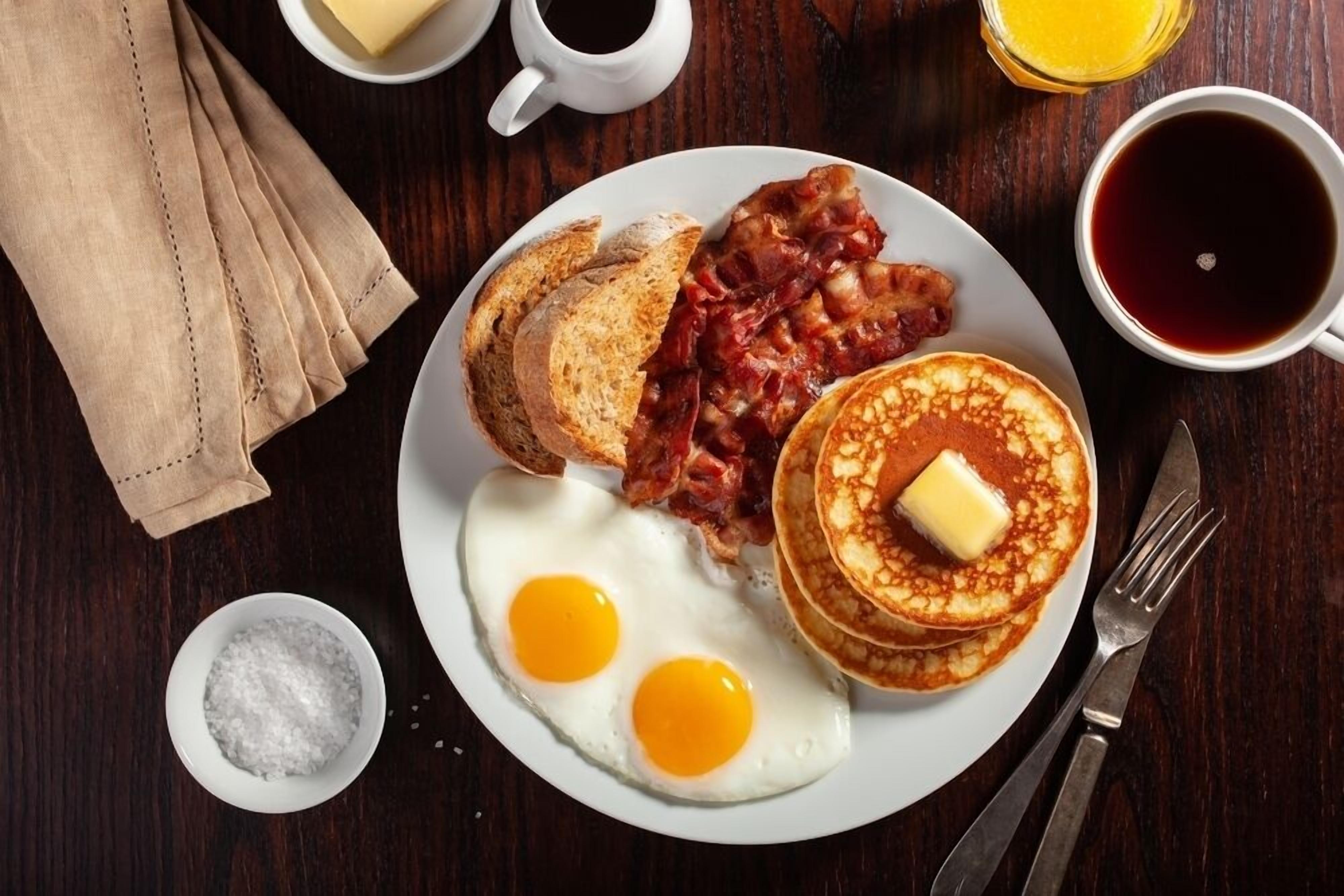 Un plato de desayuno con huevos, tocino, tostadas y panqueques sobre una mesa de madera.