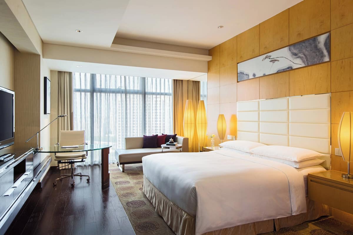A hotel room with a bed, a sofa, a desk, a television, and a large window with curtains.