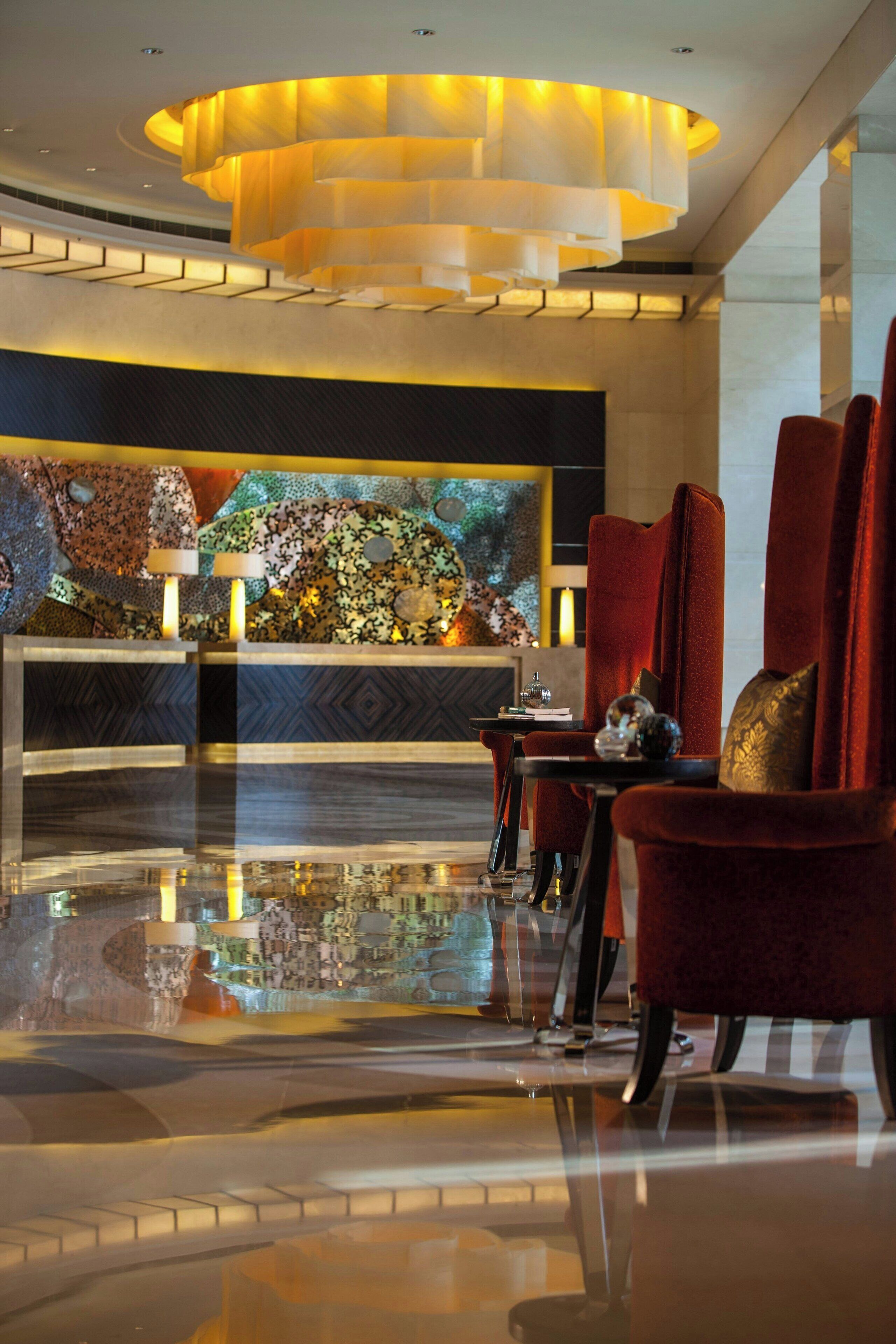A modern lobby with a reflective floor, a large decorative wall, and red upholstered chairs.