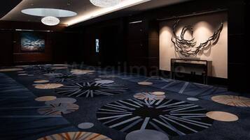 Un hall d’hôtel moderne doté d’une vaste zone recouverte de moquette, de plusieurs lustres et d’une sculpture murale.