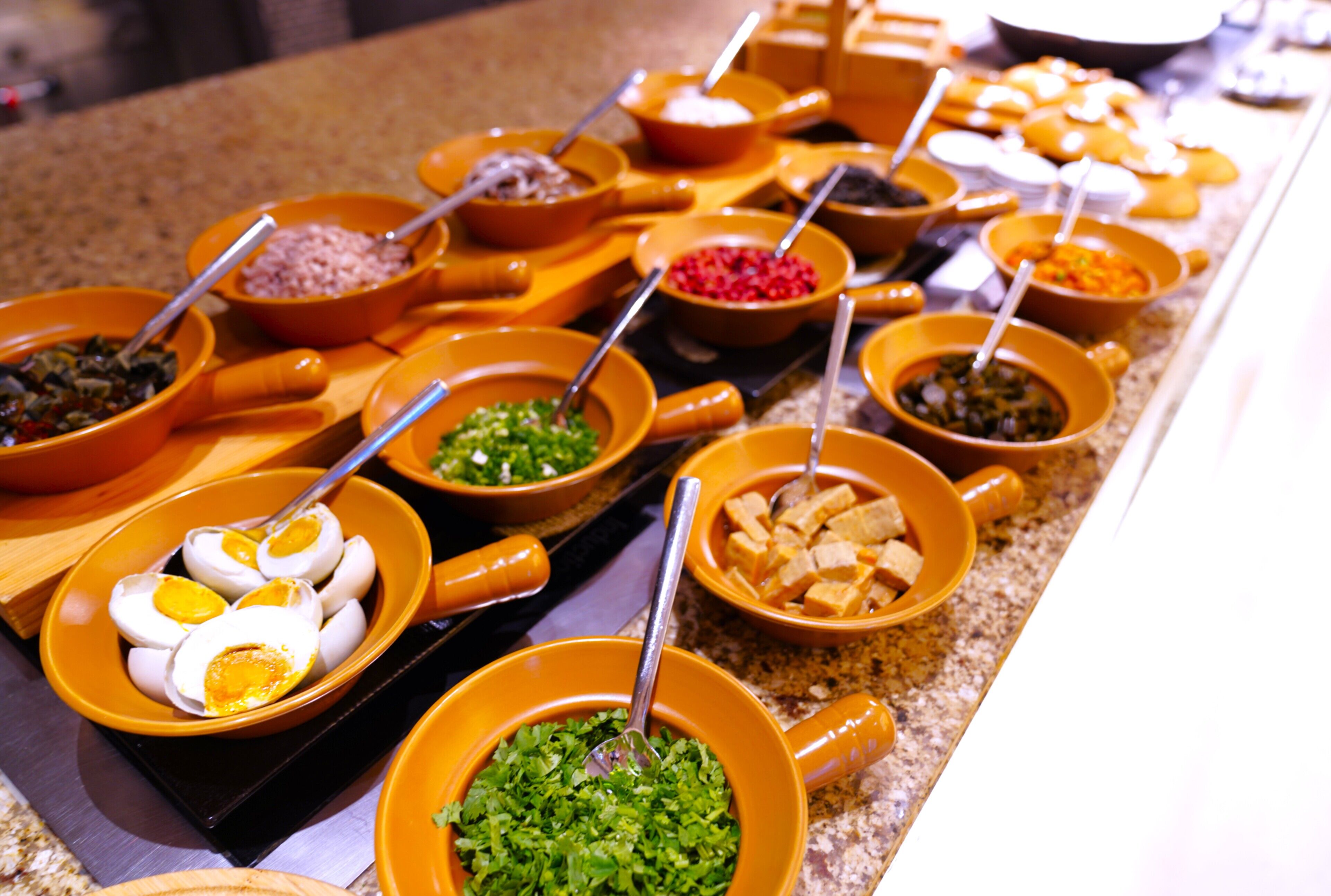 Ein reichhaltiges Buffet mit verschiedenen Speisen in orangenen Schüsseln, darunter Eier, Gemüse und weitere Gerichte.