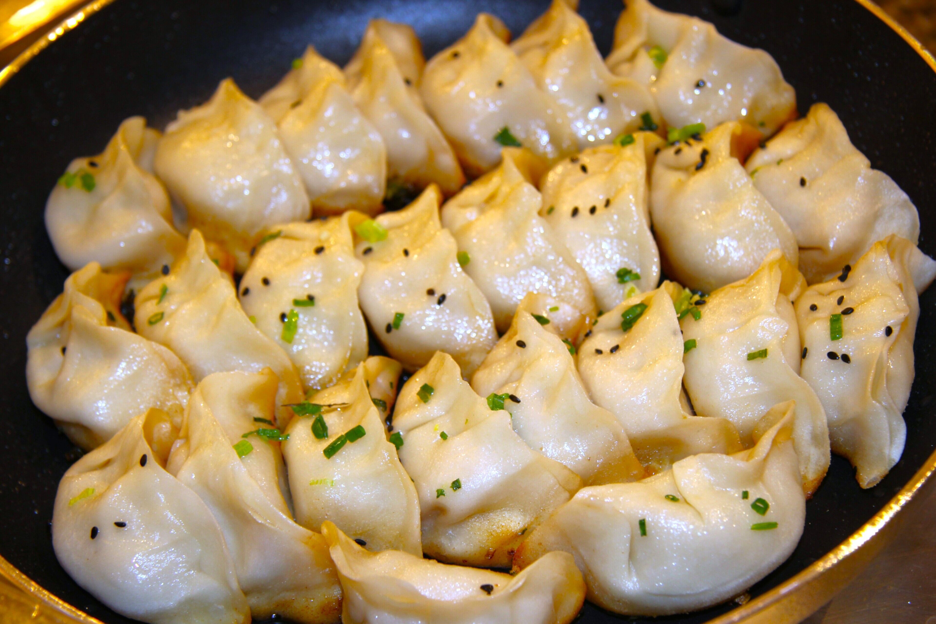 Gros plan d’une poêle remplie de raviolis, décorés de graines de sésame et d’oignons verts hachés.