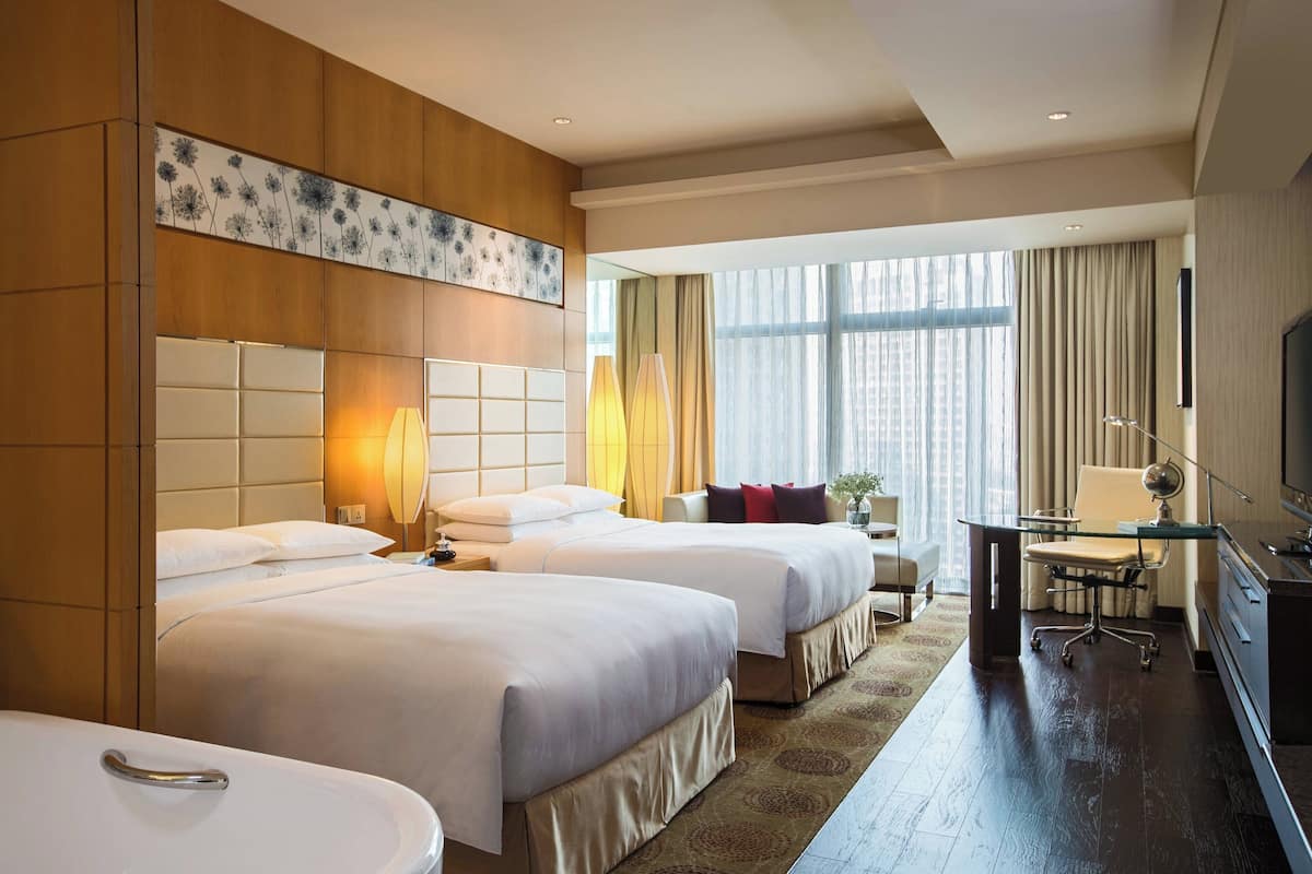 A hotel room with two beds, a desk, a chair, a TV, and a large window with curtains.