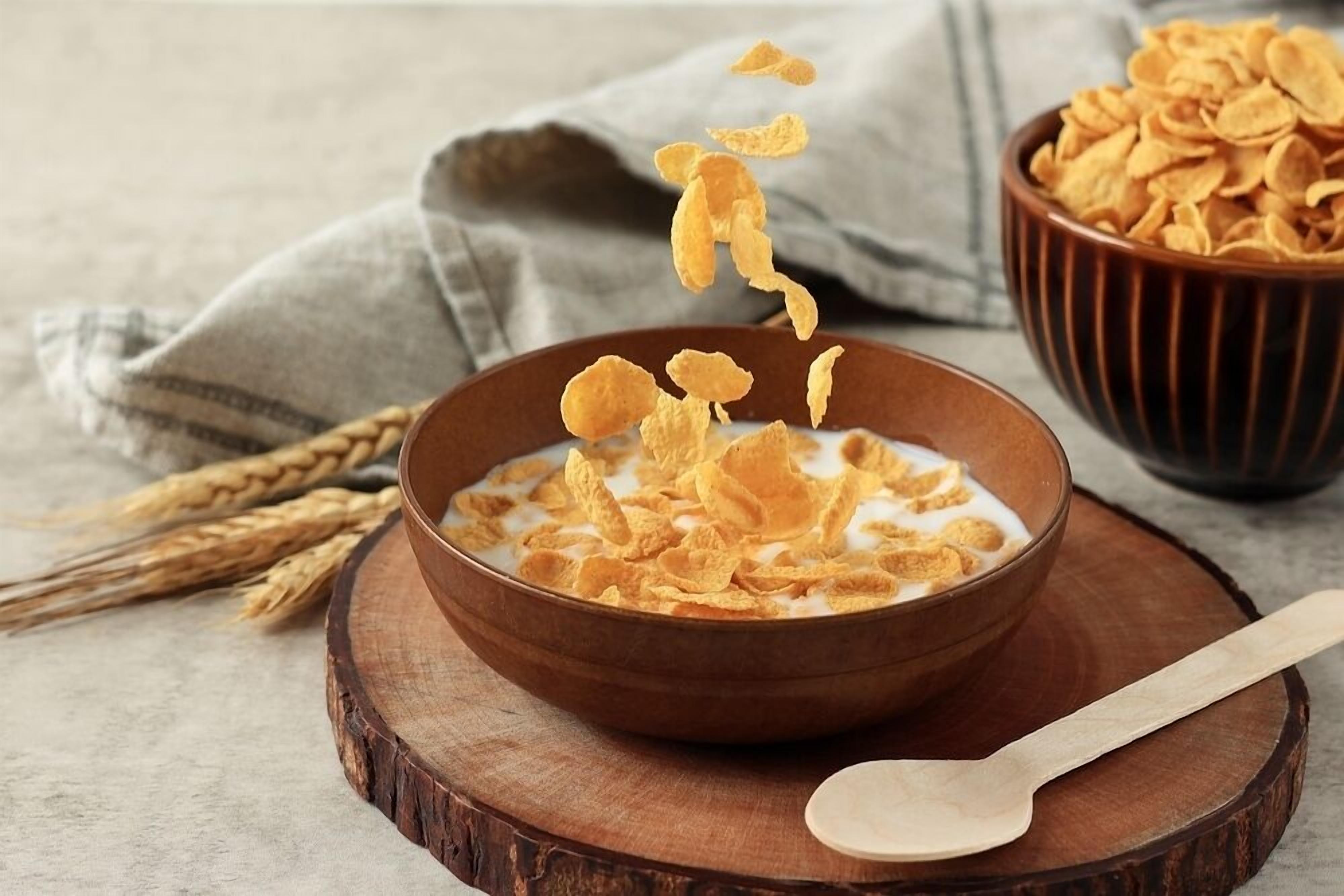 Un bol de cereals amb flocs sobre una taula de fusta, una cullera i una tovalla de tela.