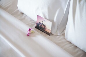 A neatly made bed with a pillow, a welcome card, and a small flower. - Emeraude Classic Cruises (Tuan Chau)