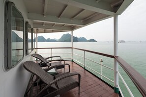 A covered deck with wicker chairs and a table, overlooking calm water and distant mountains. - Emeraude Classic Cruises (Tuan Chau)