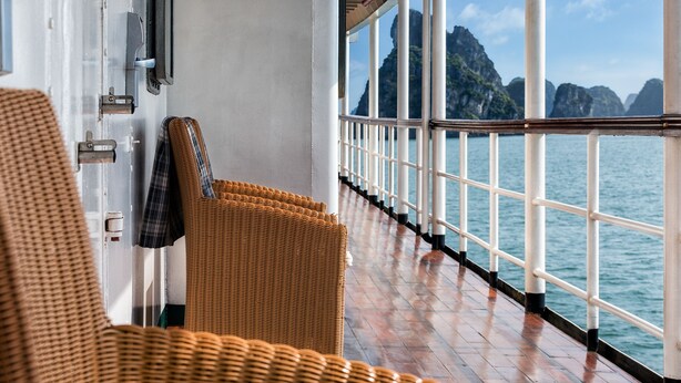 A corridor with wicker chairs, a railing, and a view of the sea and mountains.