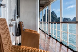 Un couloir agrémenté de fauteuils en osier, d’une rambarde et offrant une vue sur la mer et les montagnes.