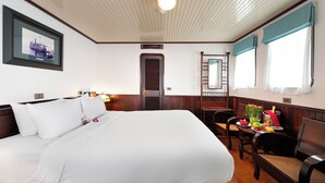 A hotel room with a large bed, a dining table with chairs, a small table with a vase and fruit, and a framed picture on the wall.
