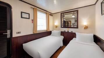 A hotel room with two single beds, a window with curtains, a framed certificate on the wall, and a mirror with wall sconces.