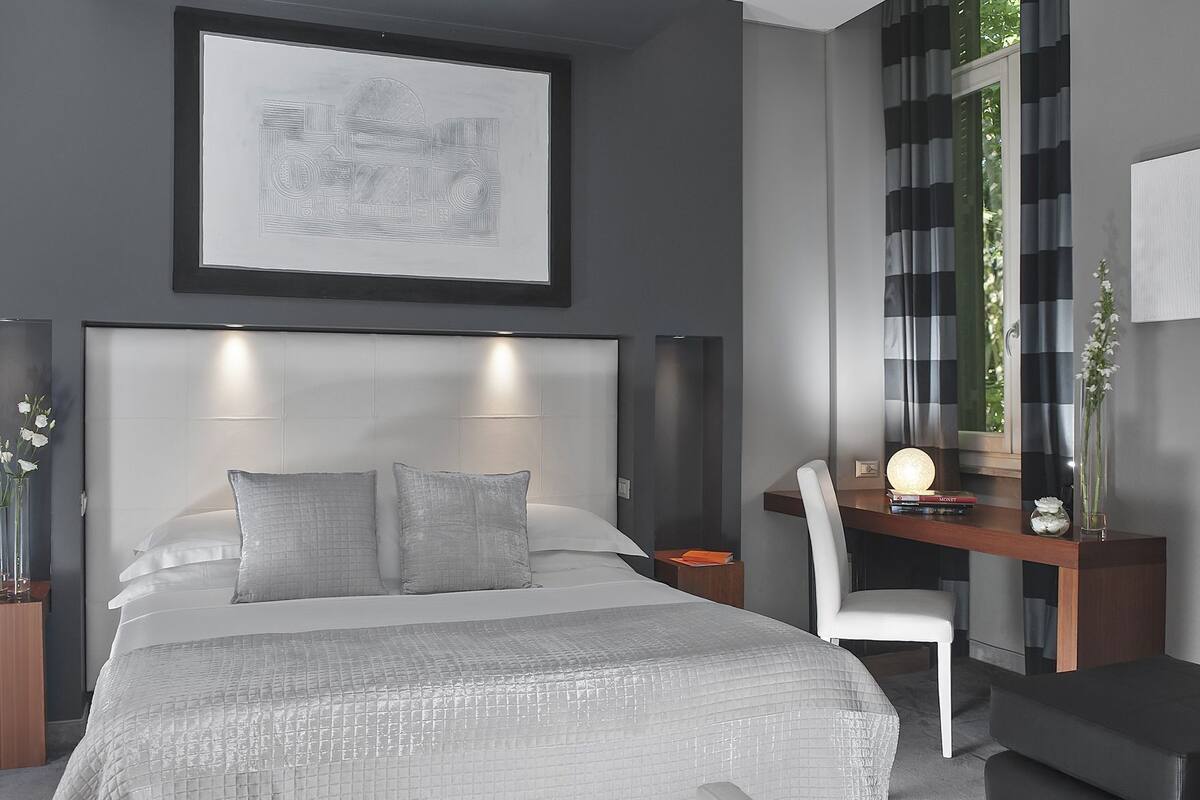 A modern bedroom with a large bed, a desk, a chair, and a framed artwork above the bed.