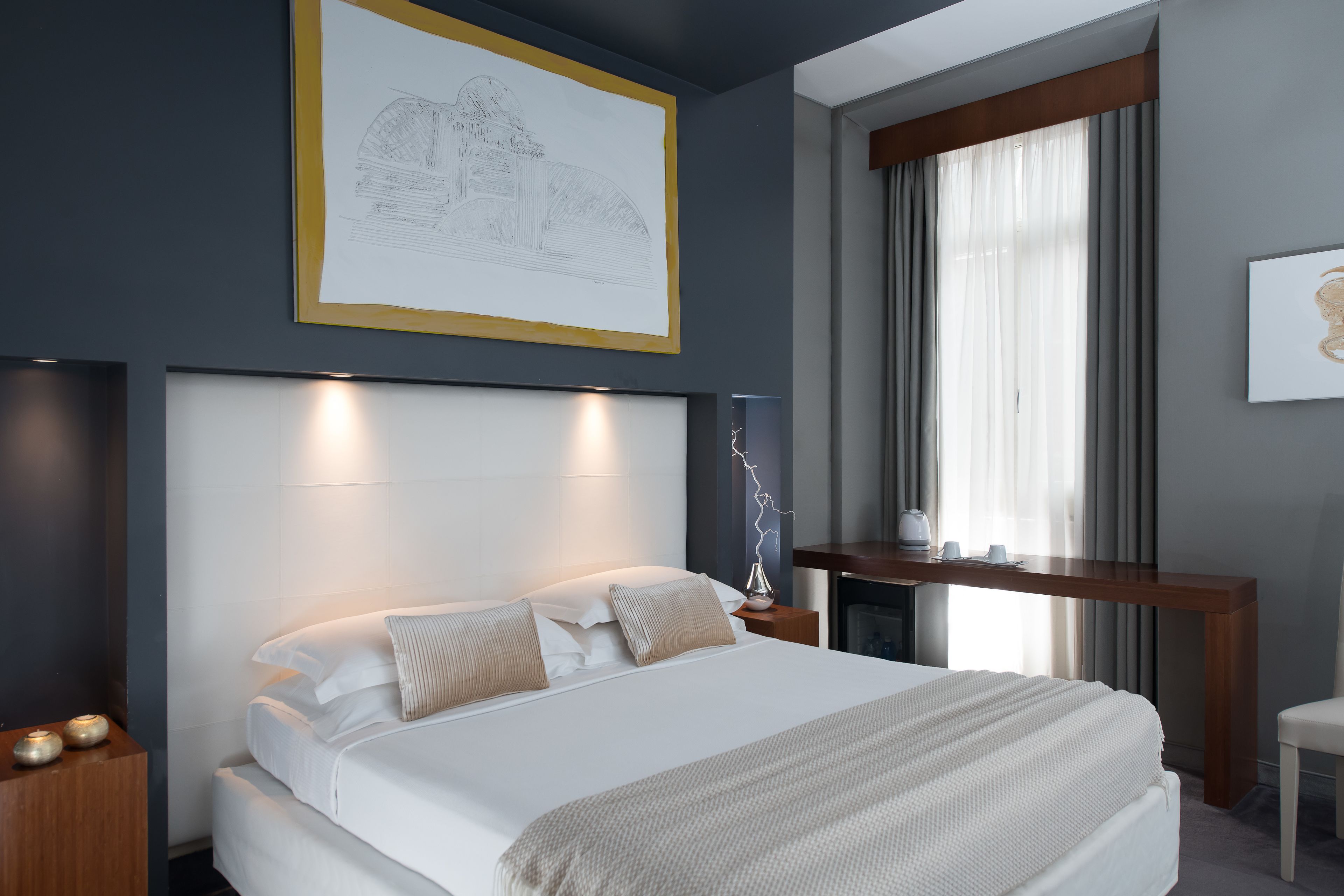 A modern hotel room with a large bed, bedside tables, a desk, and a window with curtains.